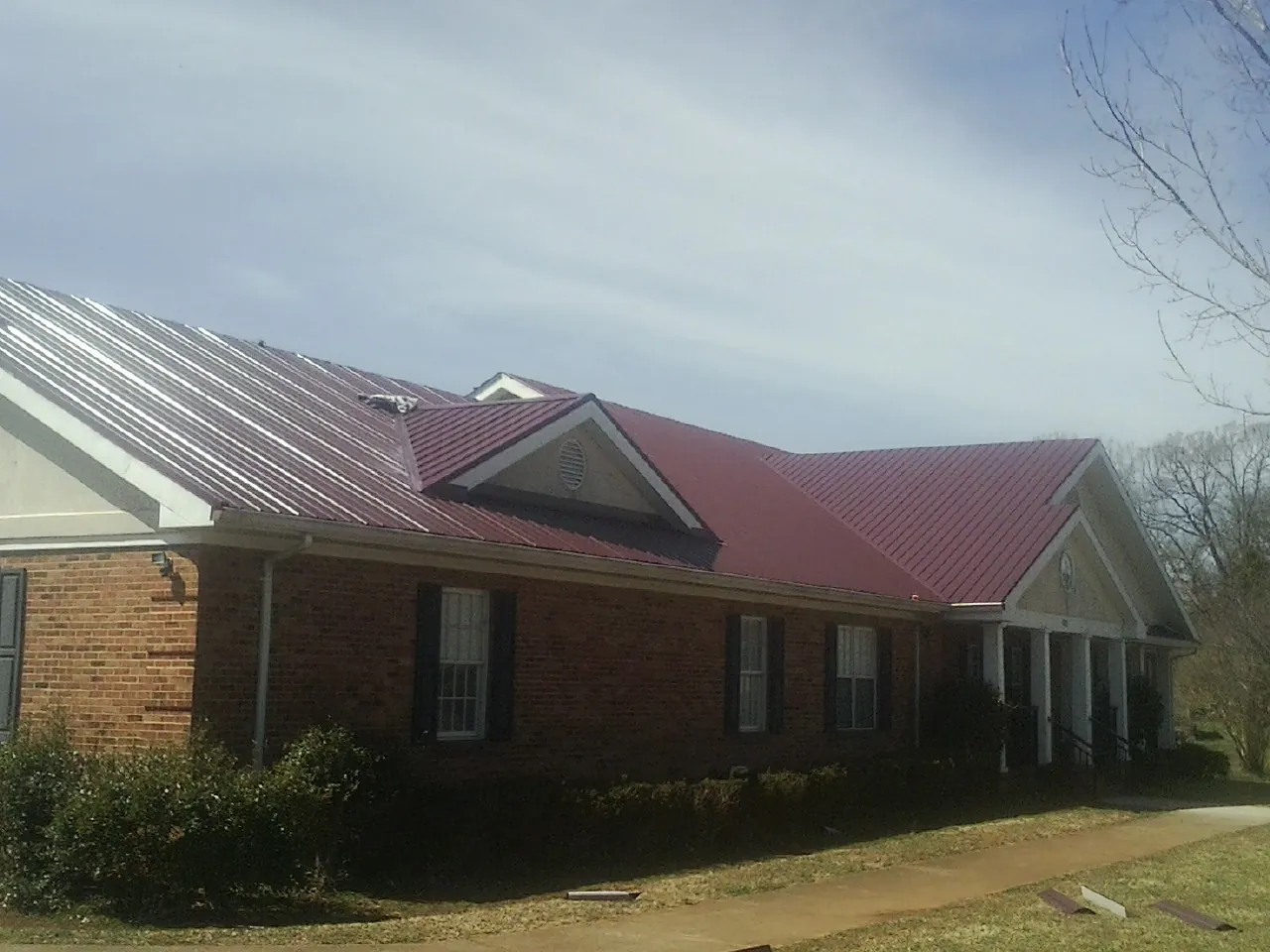 Red metal roof with gabled entries on a long brick building, from a Hail Damage Roof Repair job in Lecanto