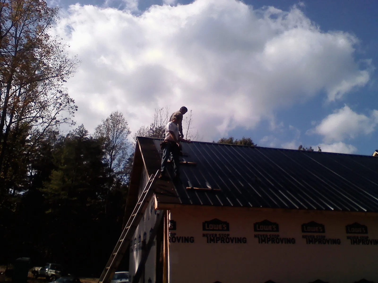 Roofer fastening dark metal panels high against a cloudy sky, from a Roof Inspection job in Lecanto