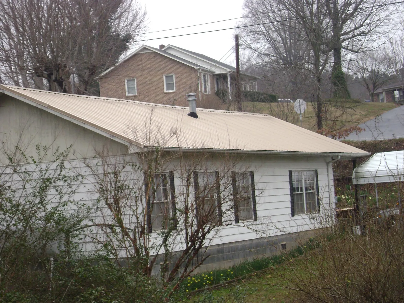 Tan metal roof on a white sided house set into a hillside — Commercial Roofing by Roofing Brothers in Lecanto